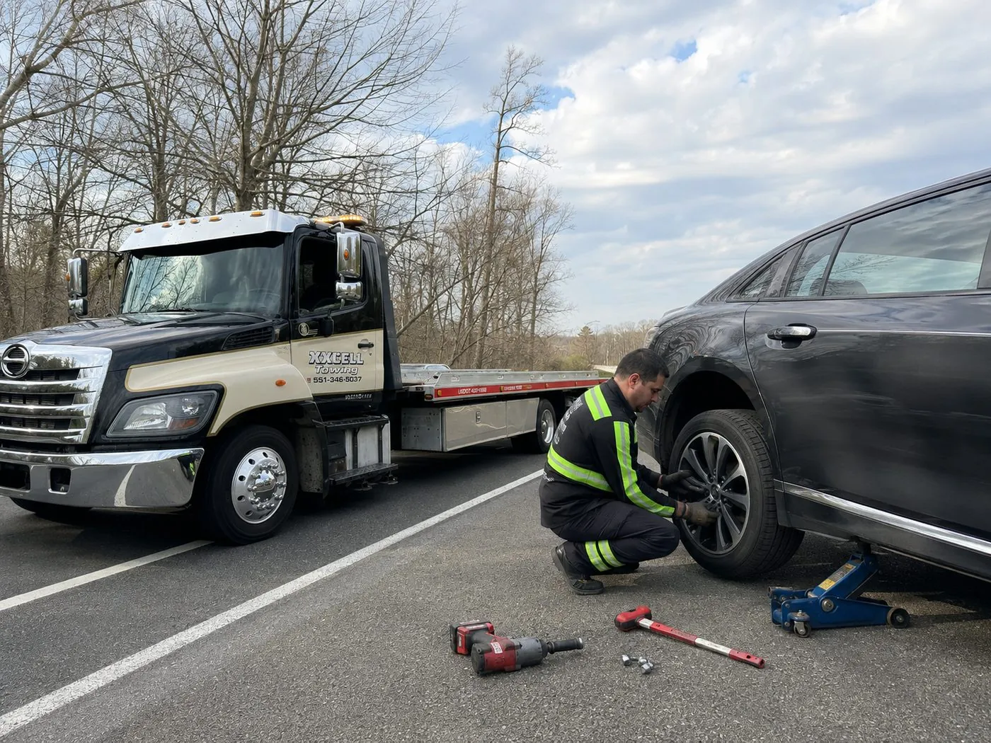 XXCELL Towing technician changing a flat tire roadside with a floor jack in Bergen County NJ